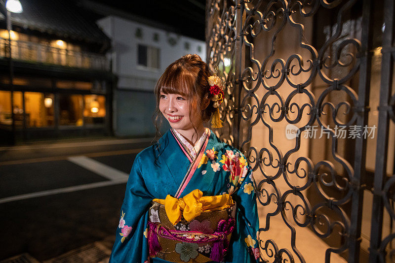身着Furisode和服的年轻女子在“Seijin Shiki”成人礼之夜参观日本传统村庄
